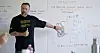 A man stands by a whiteboard with handwritten notes, sketches and diagrams in a classroom setting.